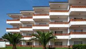 Un hôtel à plusieurs étages doté de balcons, d’un palmier et surplombant un ciel bleu azur.
