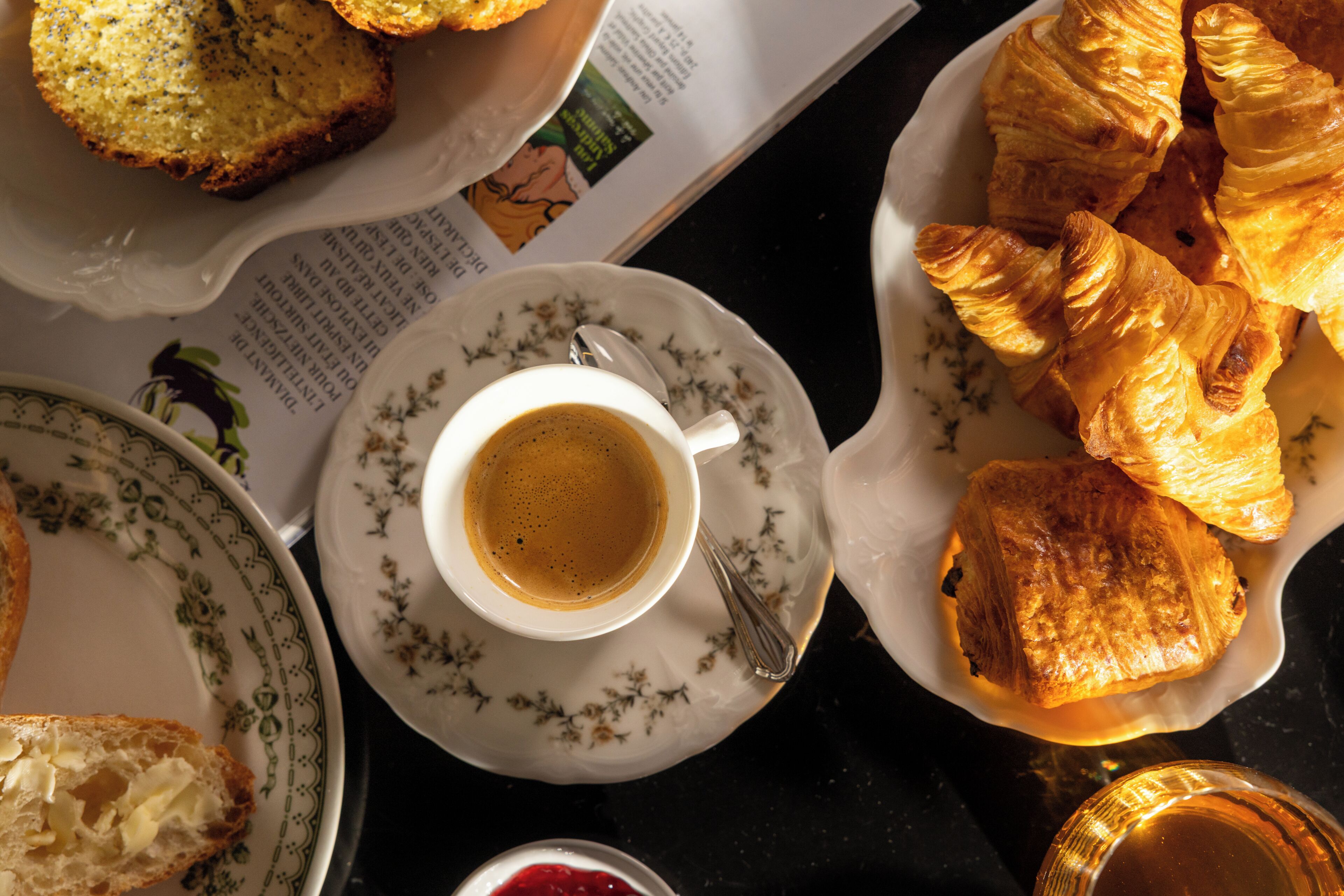 A table with a cup of coffee, croissants, and a plate of food.