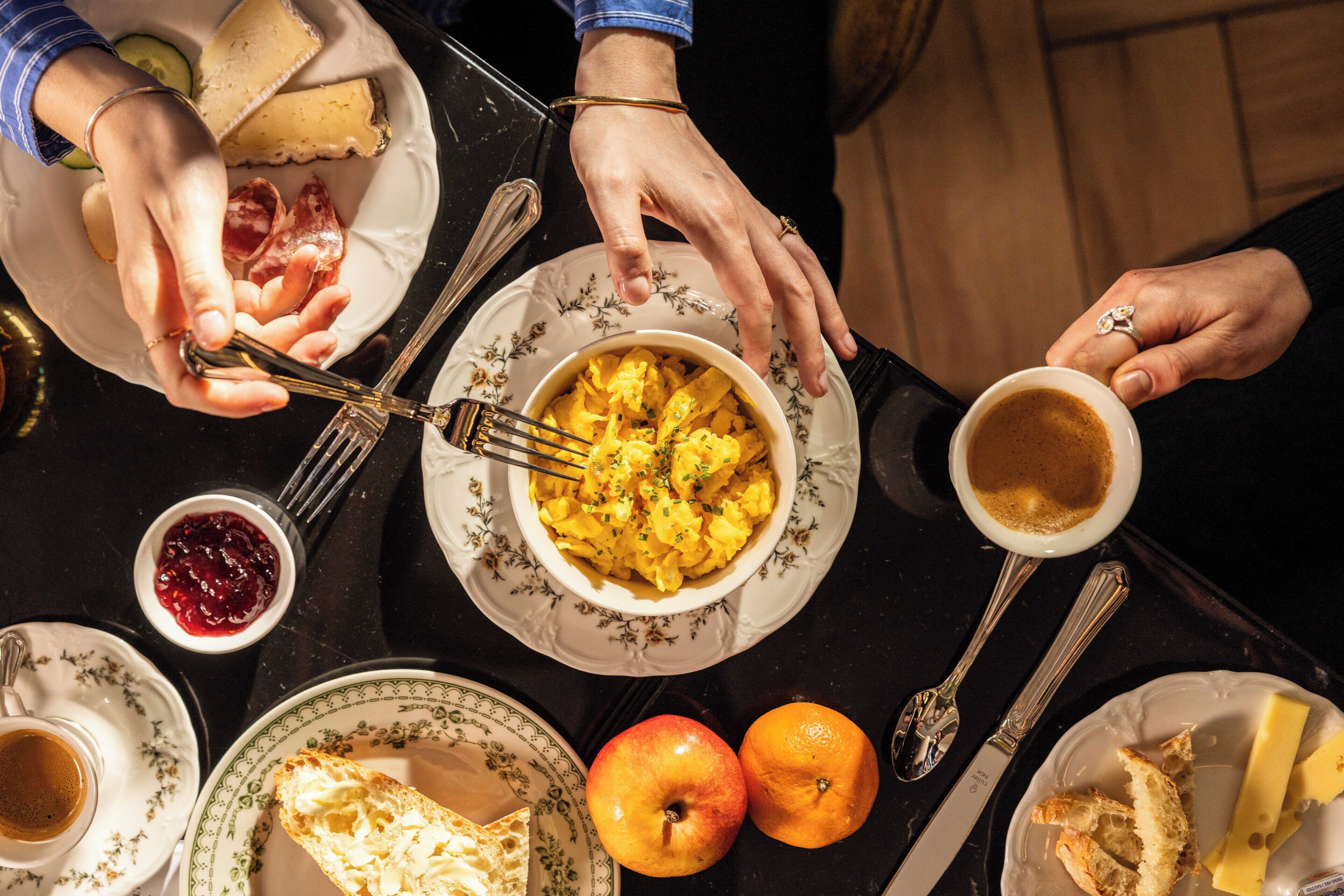 A dining table with plates of food, utensils, and a cup of coffee.