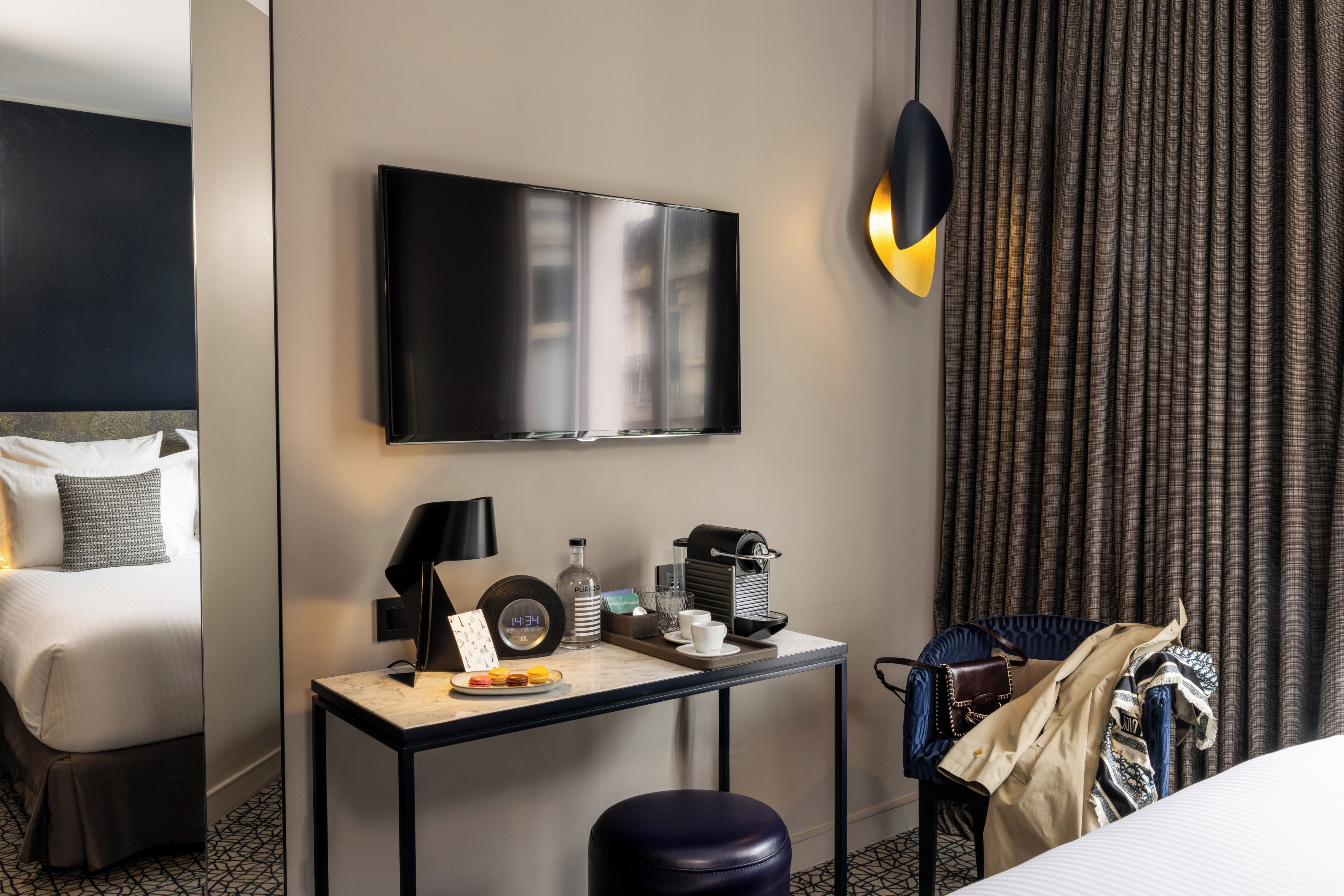 Una camera d'albergo con un letto, una scrivania con televisore a schermo piatto, una lampada, una sveglia e una sedia.