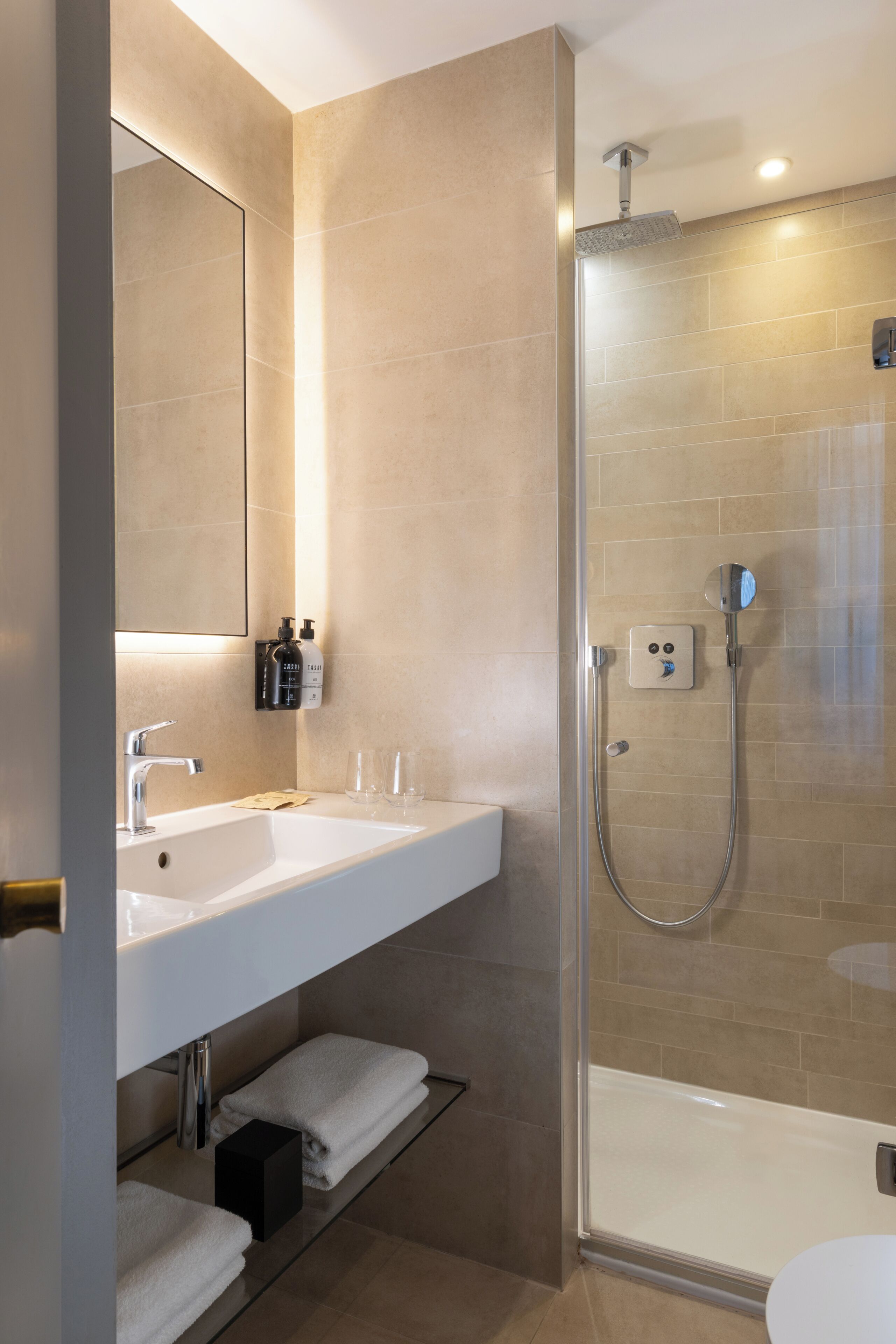 Een moderne badkamer met een douchecabine van glas, een wit wastafeltje met spiegel en keurig opgevouwen handdoeken.