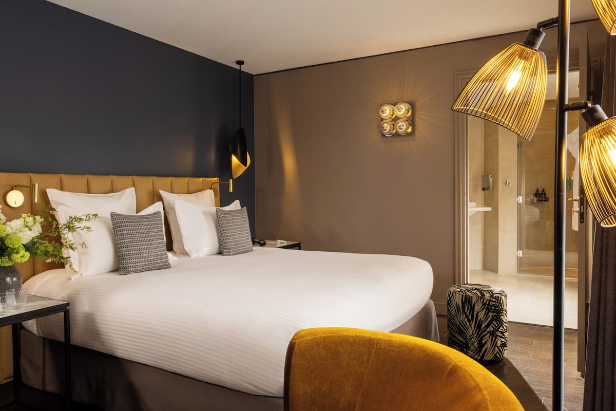 A hotel room with a large bed, bedside tables, a mirror, and a shower area.