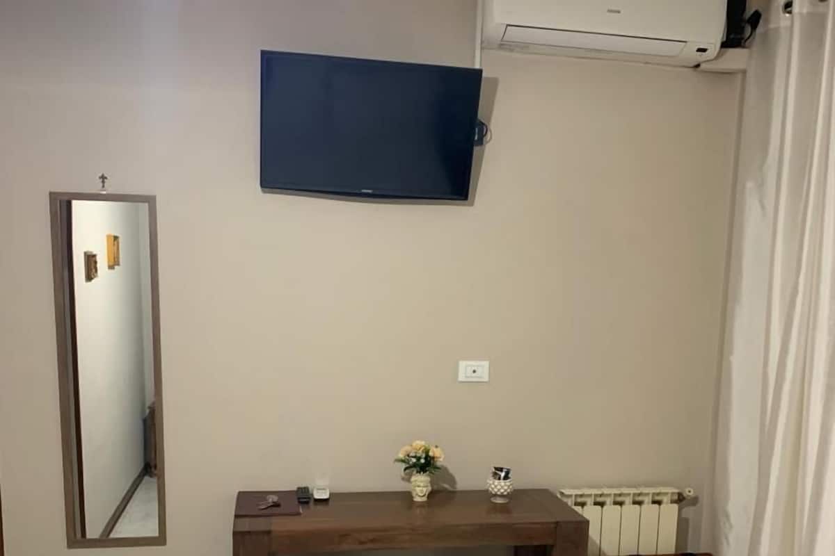 Un dormitorio con una cama, un escritorio con dos sillas, un espejo, un aire acondicionado y un radiador.