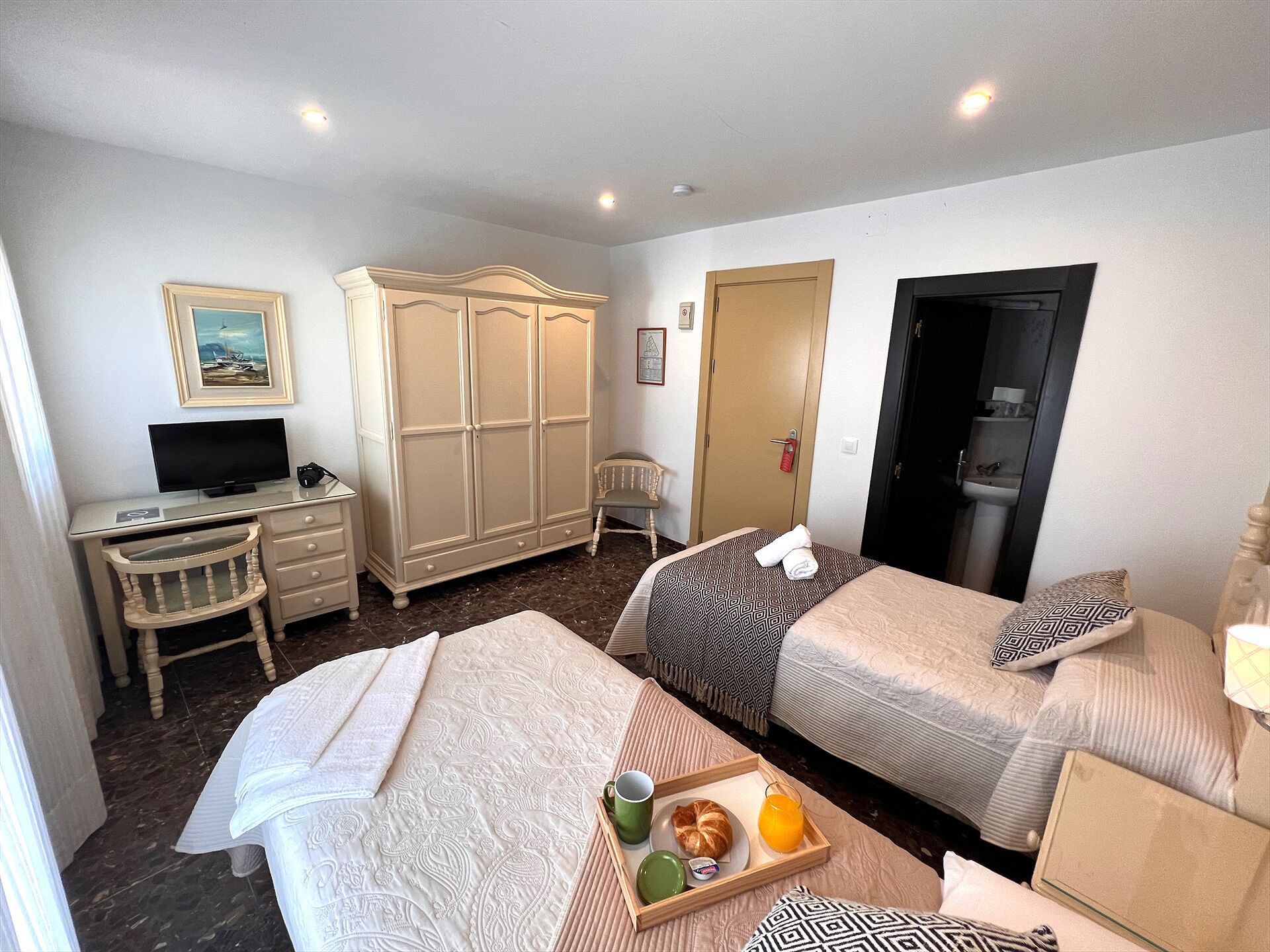 A hotel room with two beds, a desk with a TV, a wardrobe, and a breakfast tray on the bed.