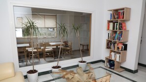 A modern living room with a glass coffee table, a wooden bookshelf, and potted plants. - Hostal La Janda (Vejer de la Frontera)