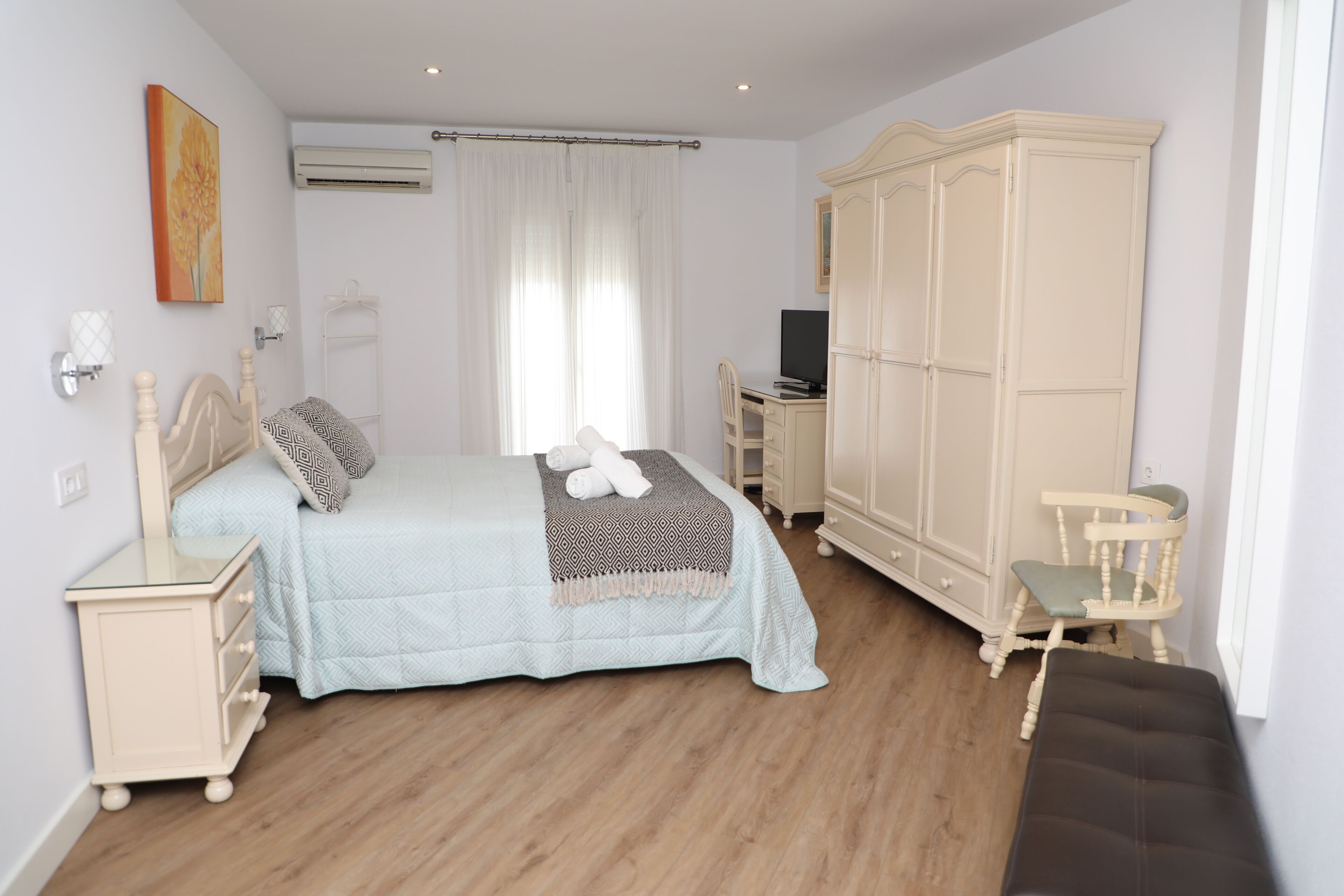Un dormitorio con cama, mesitas de noche, armario, una silla y televisor.