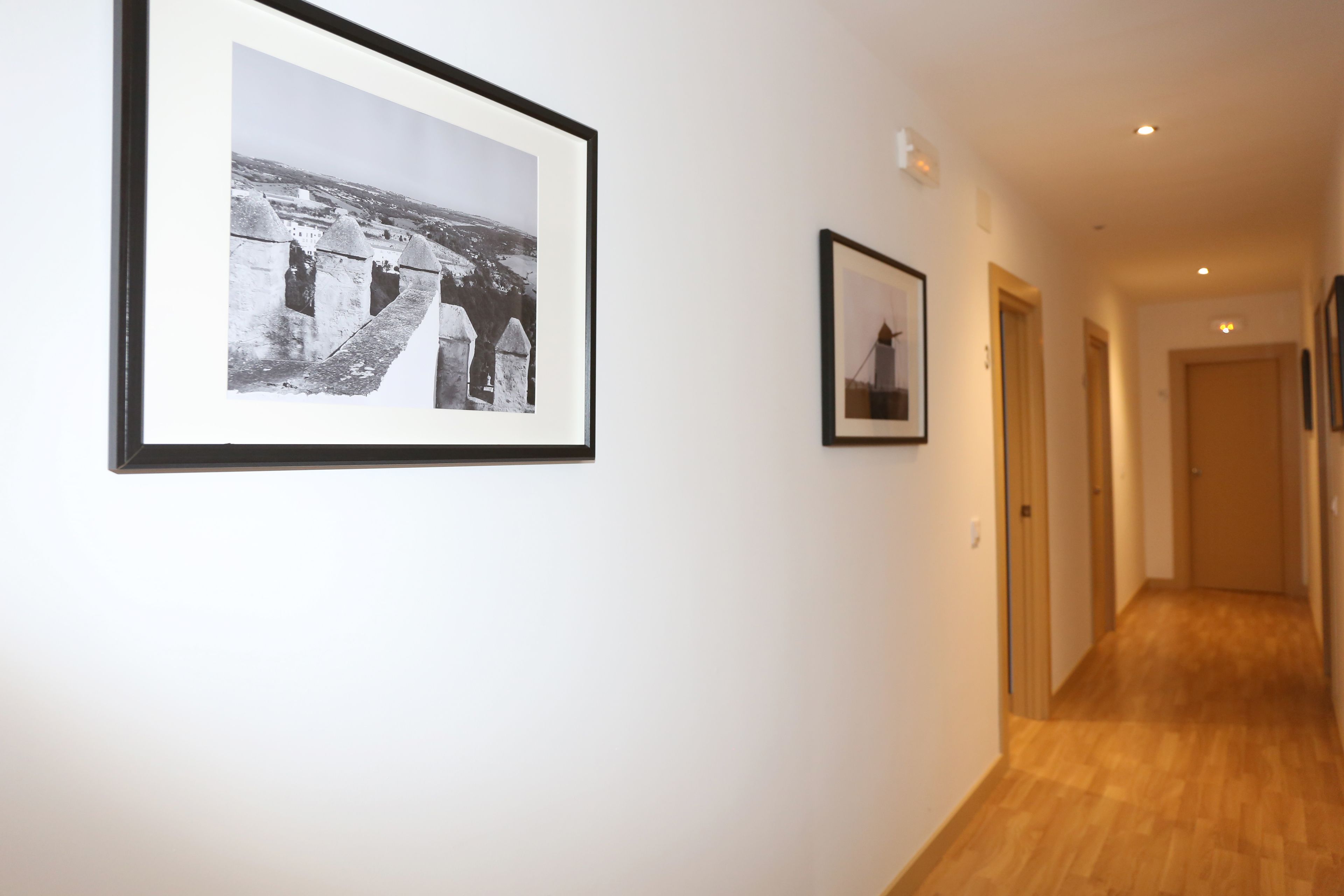 Un couloir aux murs ornés de tableaux encadrés, doté d’un plancher en bois et de portes donnant sur d’autres pièces.