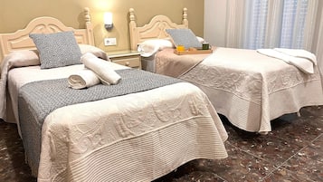 Une chambre d’hôtel avec deux lits, chacun recouvert d’une couvre-lit à motifs et agrémenté d’un oreiller. On y trouve une table de chevet avec une lampe et une tasse verte.