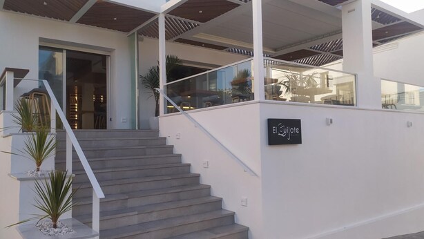 A modern building with a staircase leading to a covered area, a sign reading "El Ojote," and potted plants. - Hostal La Janda (Vejer de la Frontera)