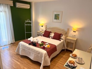 A neatly made bed with a red blanket, pillows, and towels. There are bedside tables with lamps, a small table with breakfast items, and a chair. - Hostal La Janda (Vejer de la Frontera)
