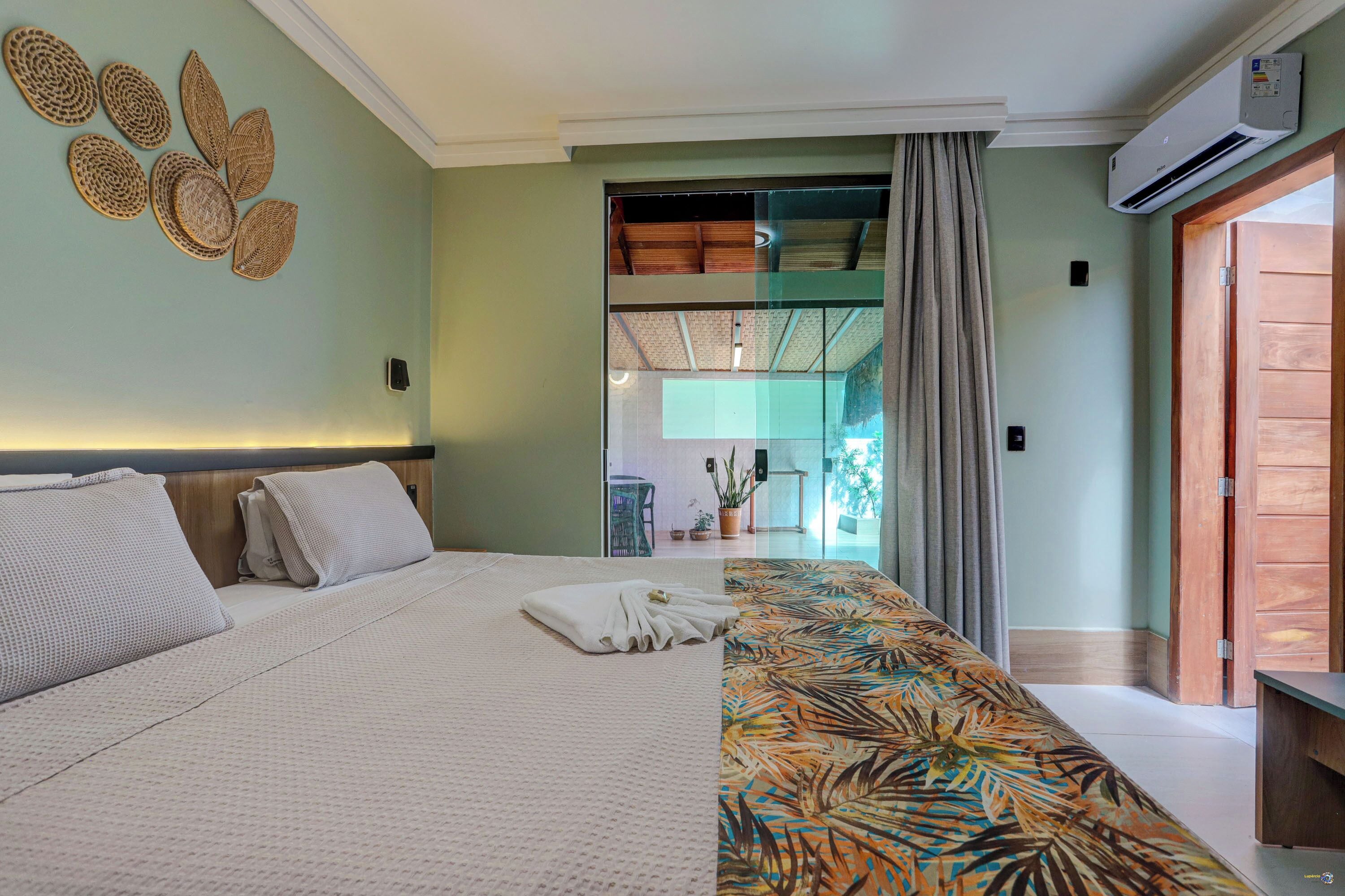 A hotel room with a bed, a patterned sofa, a wall art piece, and a view of the outside.