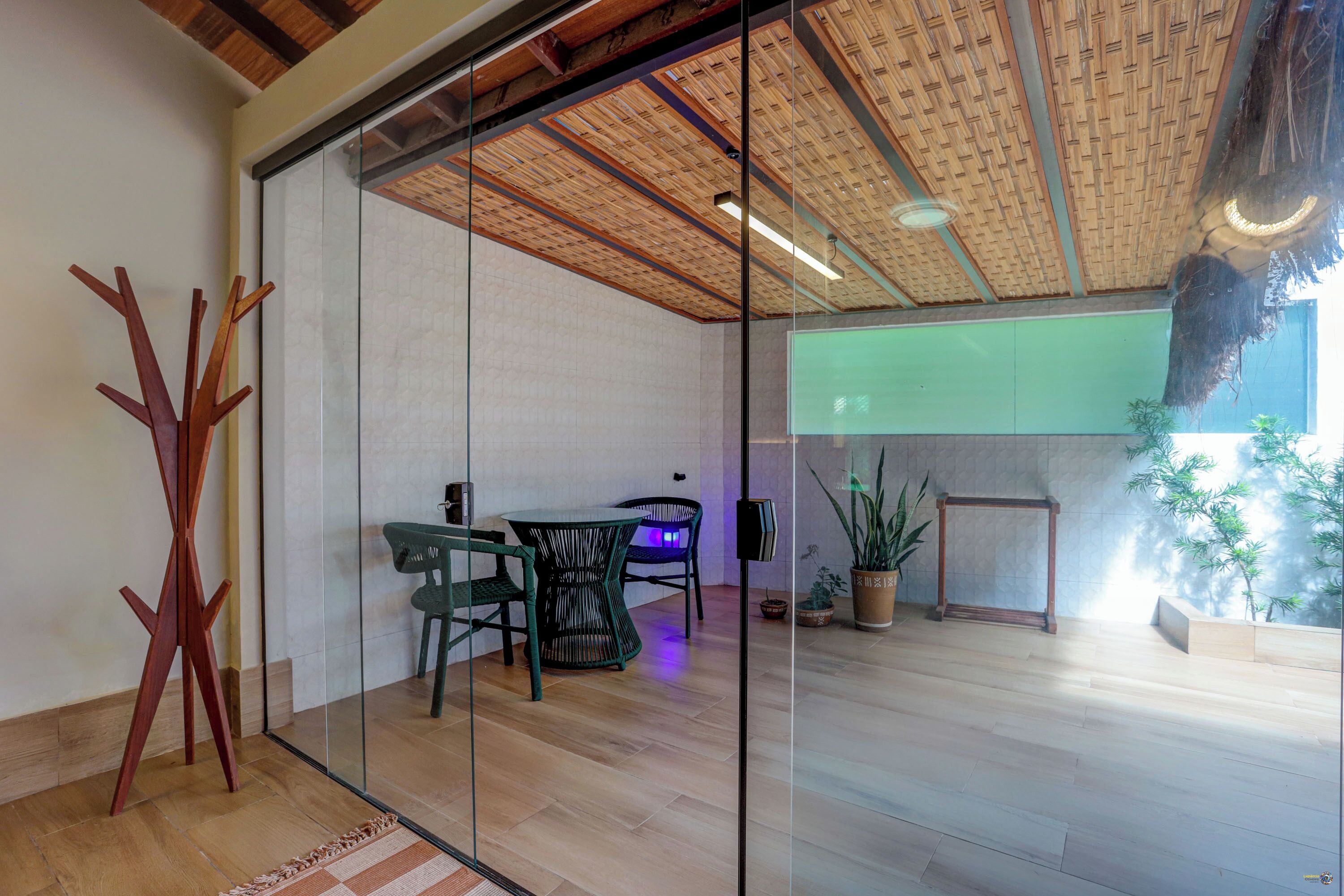 Interior moderno com divisória de vidro, soalho de madeira e zona de refeições com cadeiras e mesa.