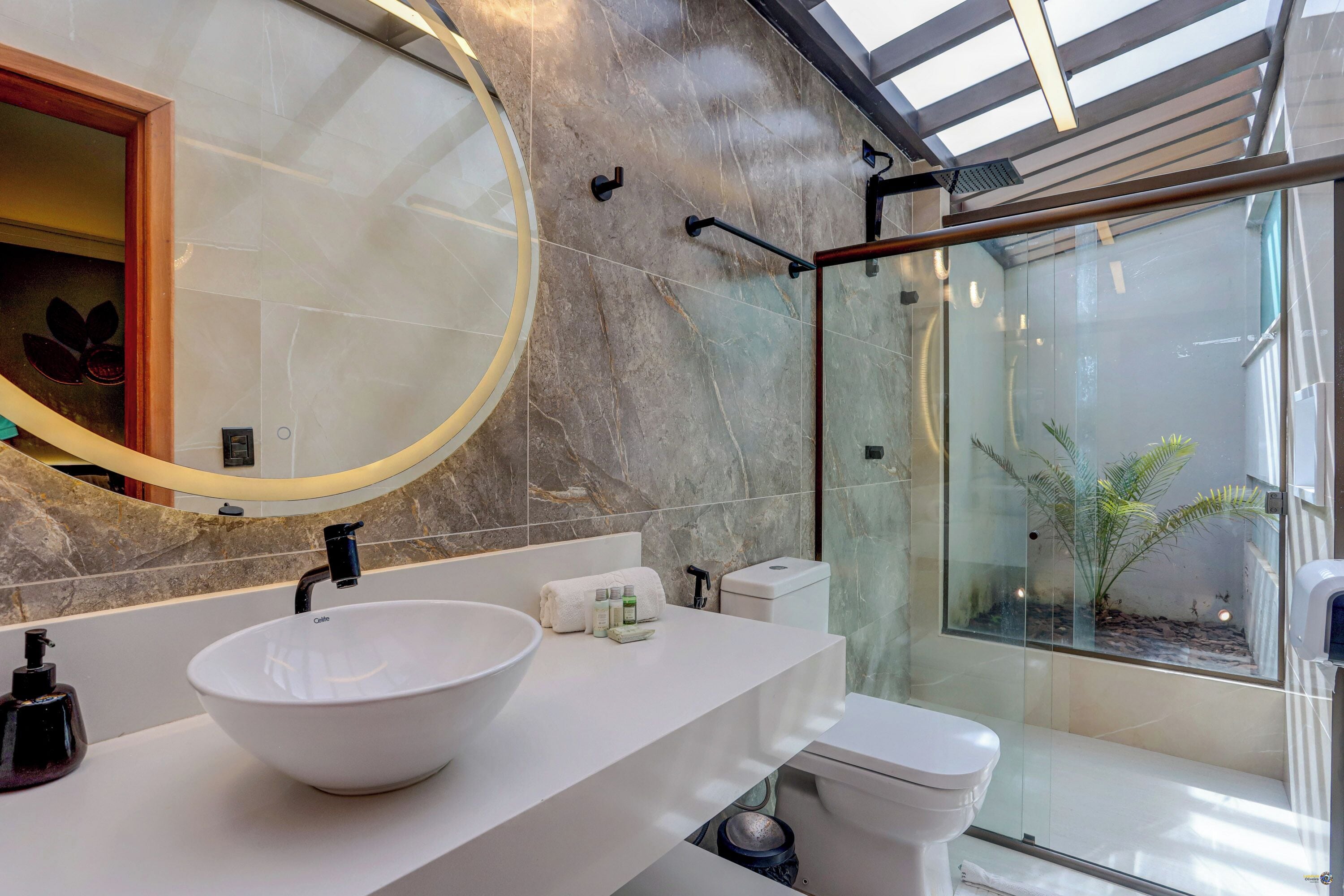A modern bathroom with a large round mirror, a white sink, and a glass-enclosed shower area.