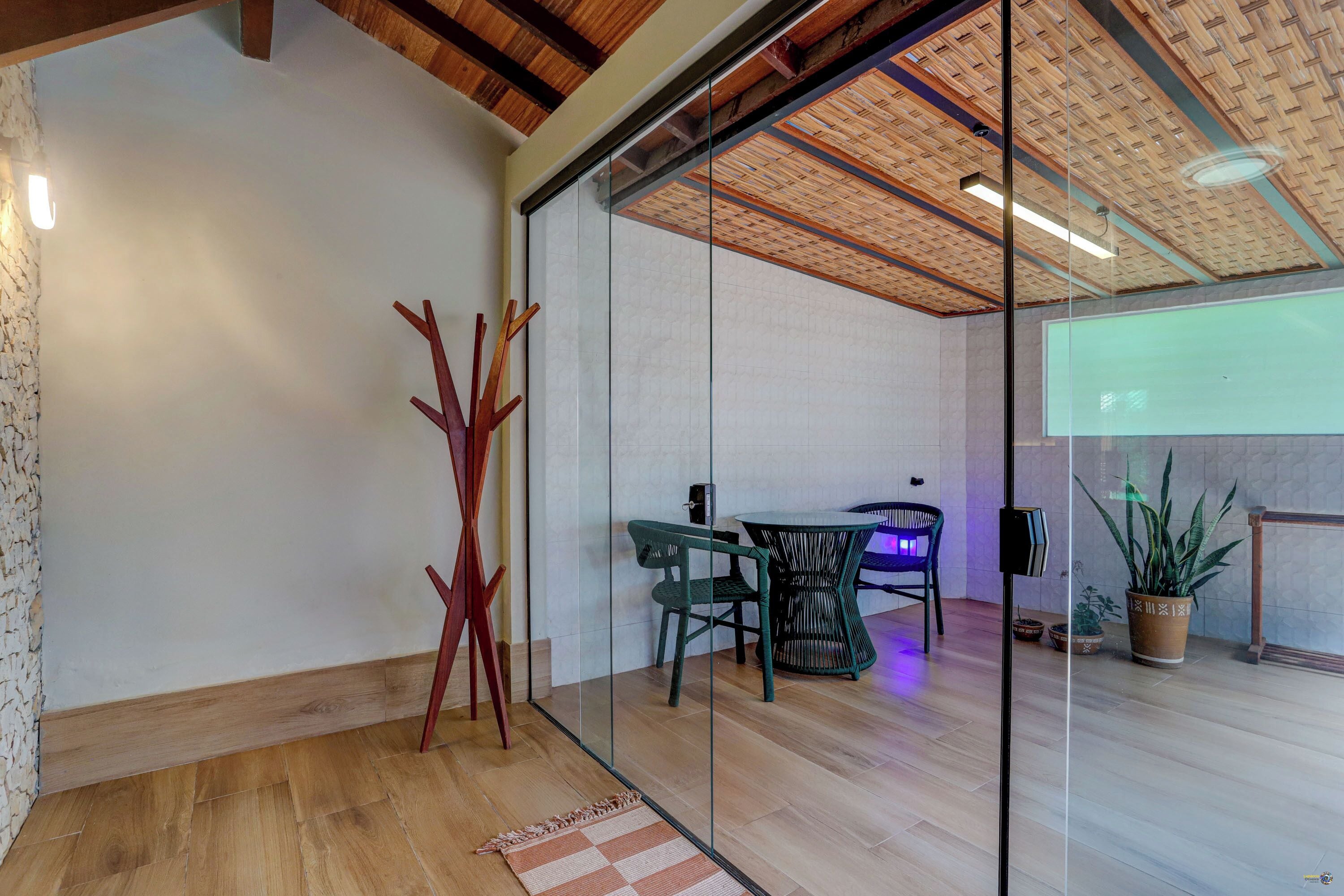A modern interior with a glass partition, wooden flooring, a dining area with chairs, and a potted plant.