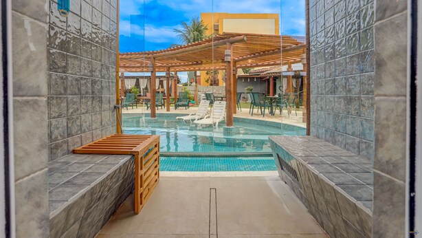 A pool area with a pergola, lounge chairs, and a wooden bench. - Pousada Praia Bela (Ilhéus)