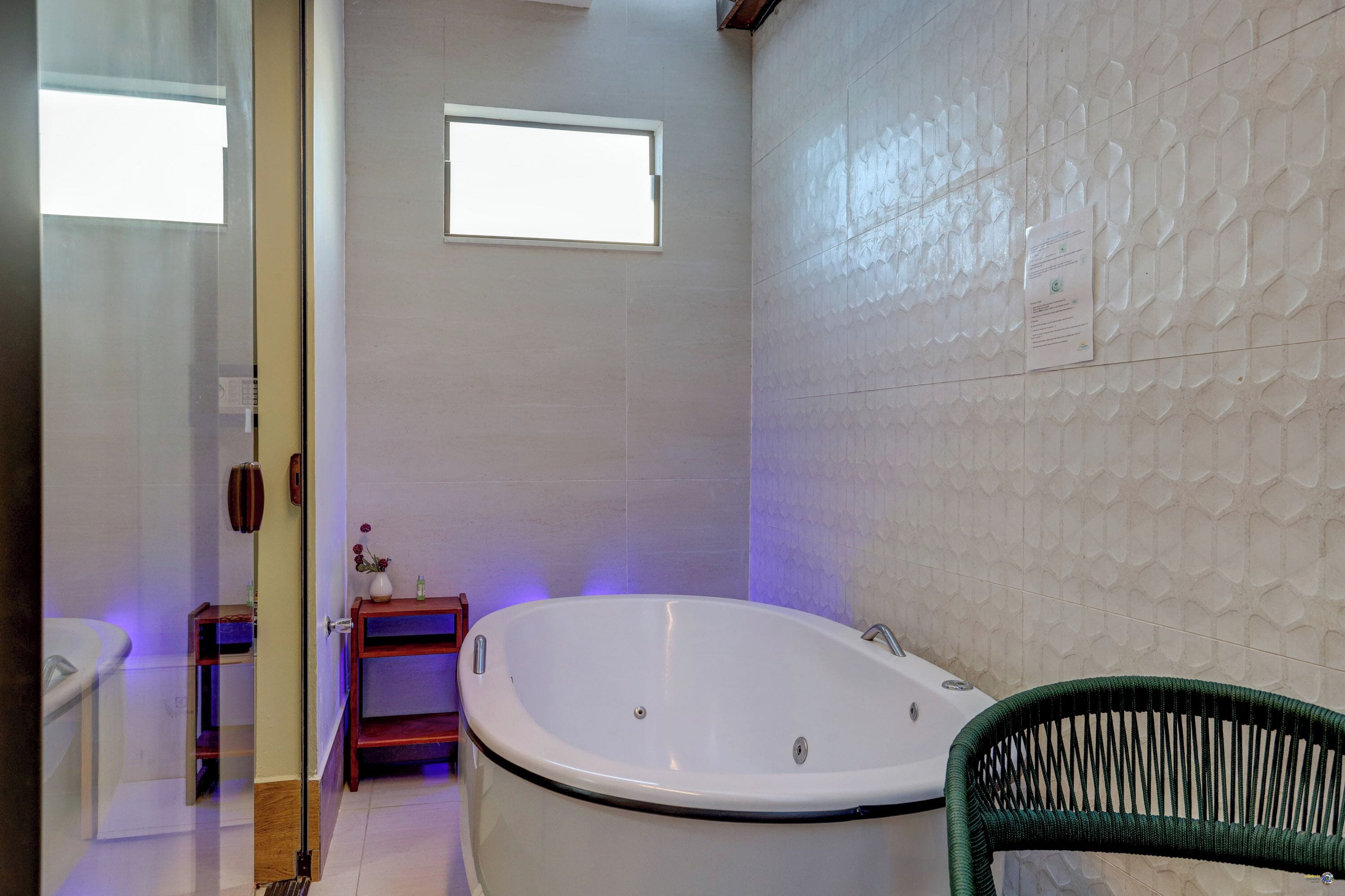 A bathroom with a bathtub, a small window, and a green chair.