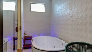 A bathroom with a bathtub, a small window, and a green chair.