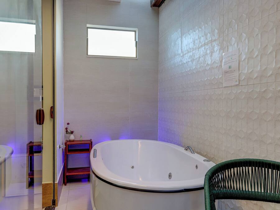 A bathroom with a bathtub, a small window, and a green chair.