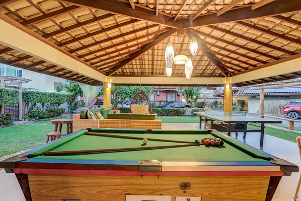Un espace piscine intérieur doté d’un plafond en bois, d’une table de billard et d’un coin salon.