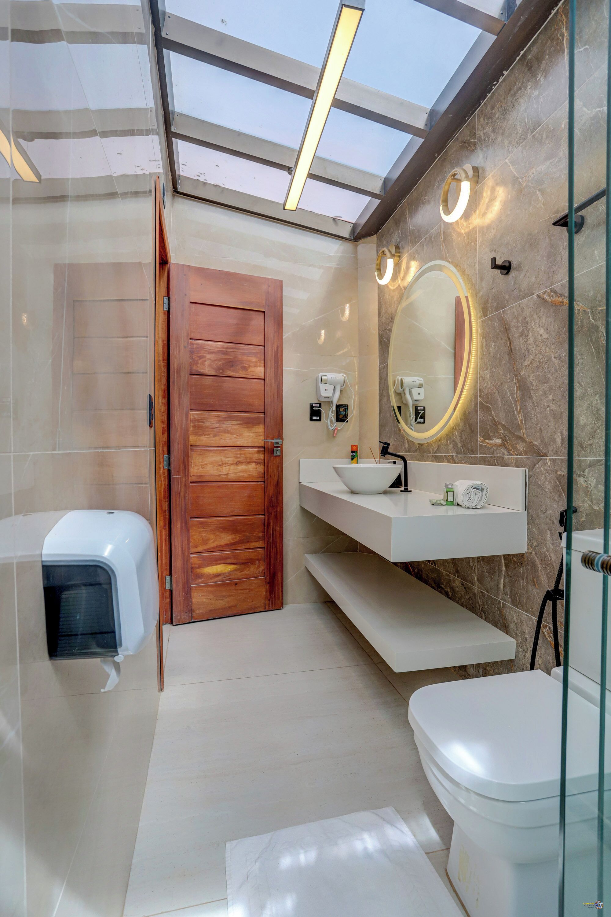 A modern bathroom with a skylight, a wooden door, a white sink, a mirror, and a toilet.