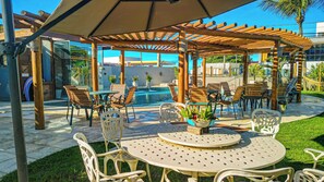 Un espacio al aire libre cubierto con mesas y sillas, una piscina y una estructura de pérgola.