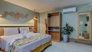 Habitación de hotel con cama, armario de madera, planta en maceta, espejo y equipo de aire acondicionado.