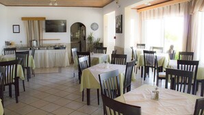 Un comedor con mesas y sillas, una cocina al fondo y un ventanal con cortinas.