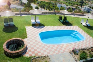 A backyard with a swimming pool, checkered patio, lounge chairs, and a fire pit.