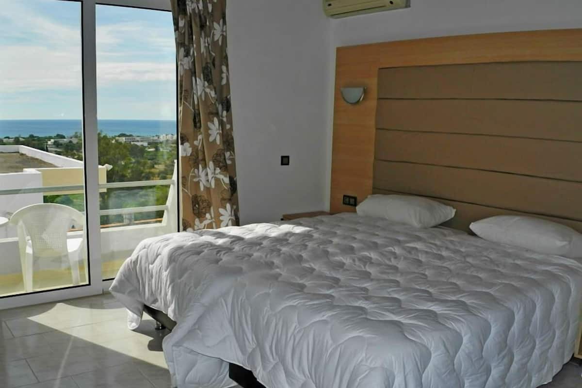 Un dormitorio con una cama grande, vista al mar y un balcón con una silla.