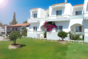A white building with balconies and a well-maintained lawn.