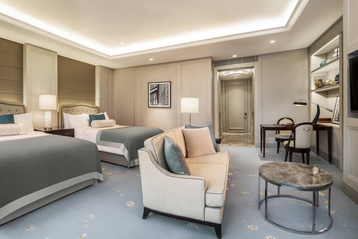 A hotel room with two beds, a sofa, a small table, and a TV.