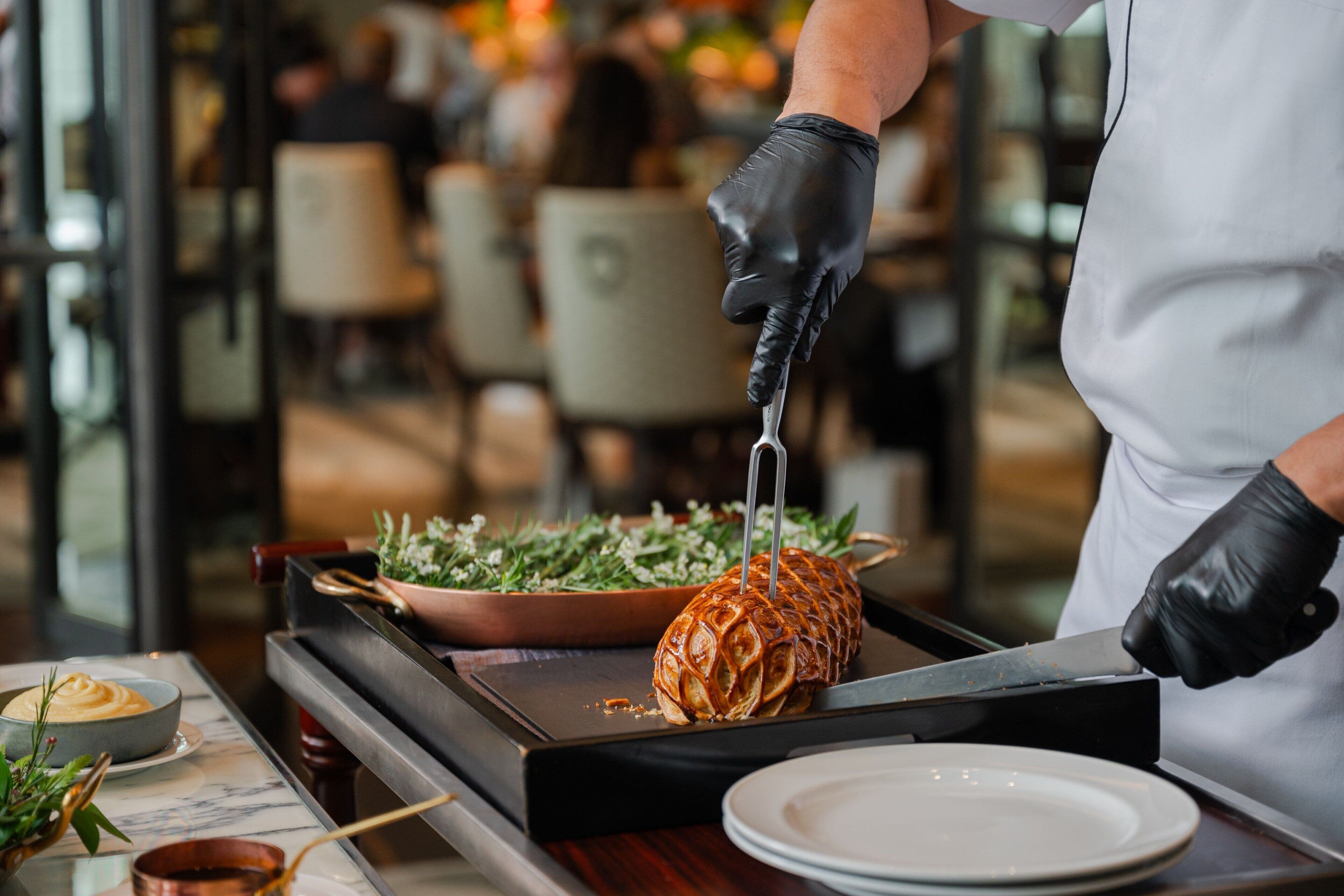 A person in a white apron and black gloves preparing food on a grill.