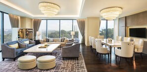 A modern hotel room with a large sofa set, a dining table with chairs, a TV mounted on the wall, and a view of the cityscape through large windows. - The St. Regis Kuala Lumpur (Kuala Lumpur)