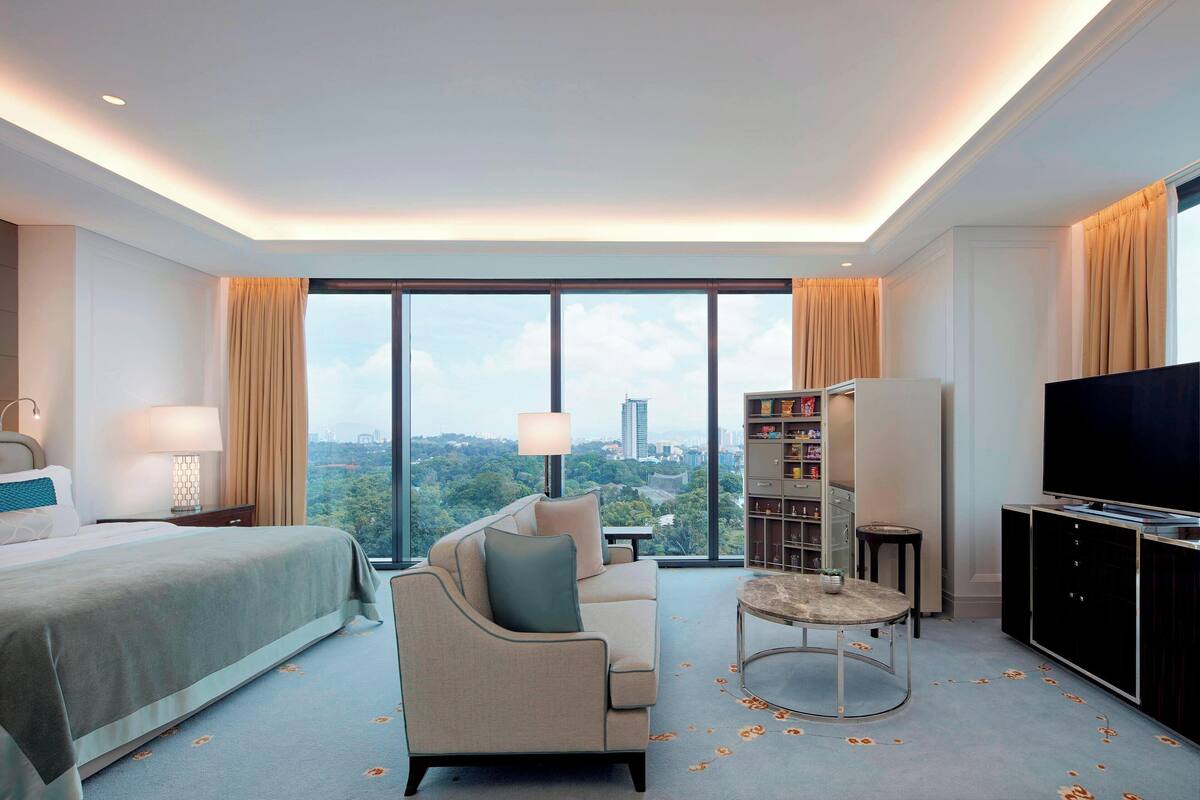 A modern hotel room with a large bed, a sofa, a TV, and a view of the city.