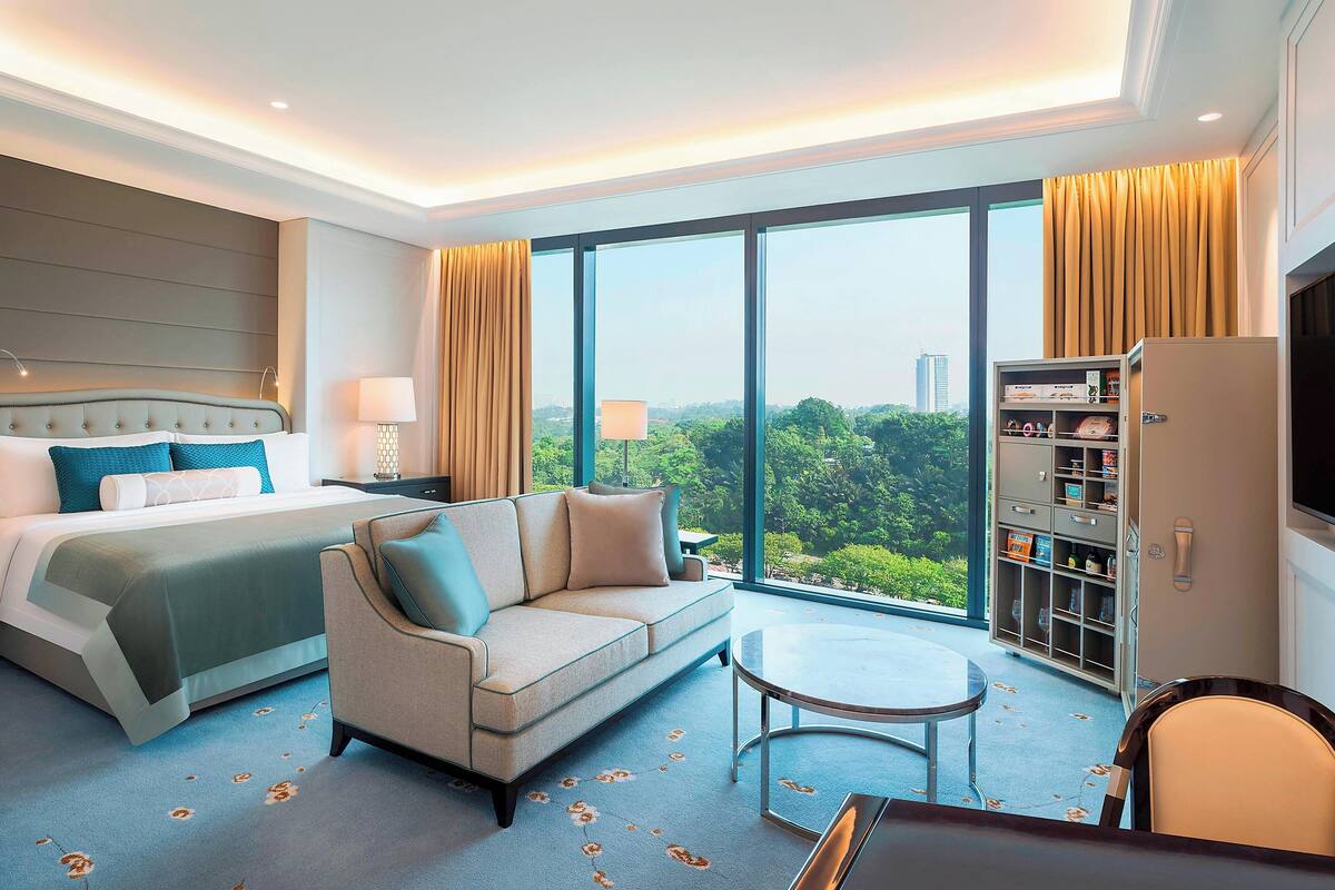 A hotel room with a bed, sofa, round table, and a minibar.