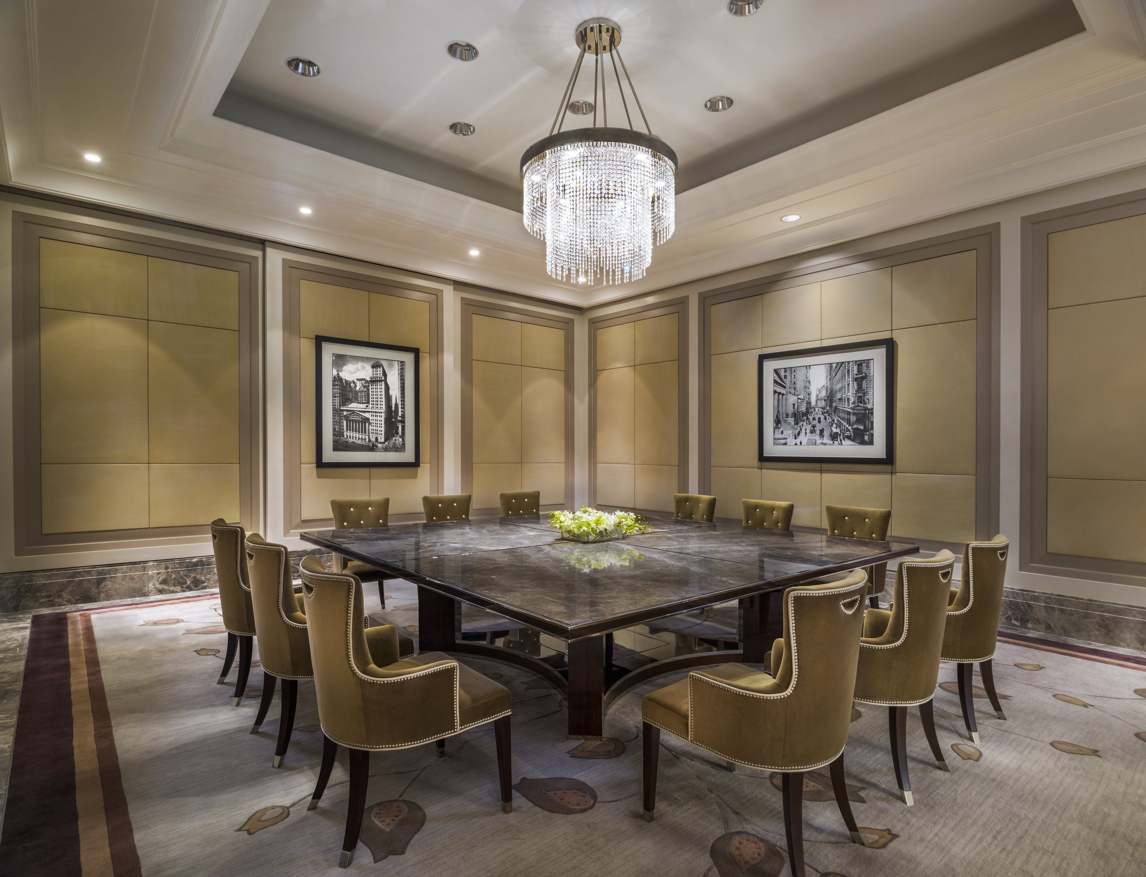 A conference room with a large table surrounded by chairs, a chandelier, and framed pictures on the walls.