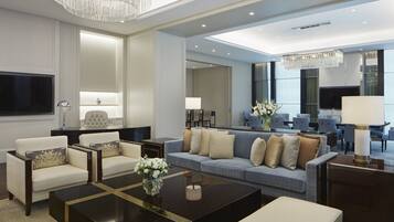 A modern living room with a sofa, armchairs, and a coffee table. There is a TV and a chandelier.
