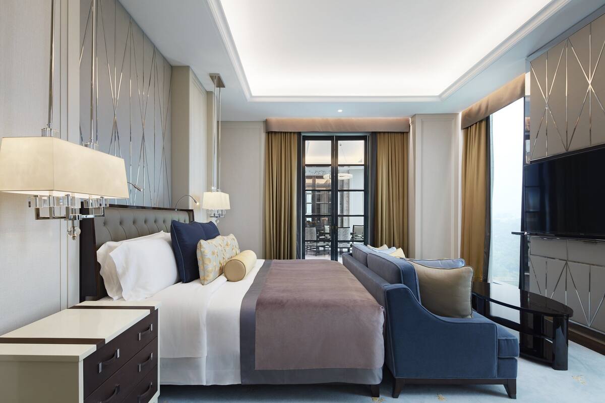 A modern hotel room with a large bed, a sofa, a TV, and a view of the city.