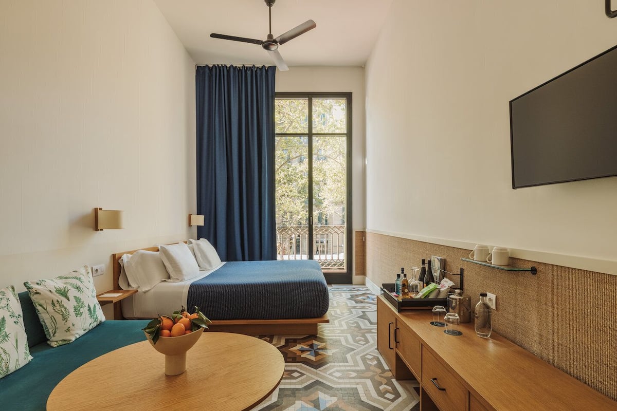 Une chambre d’hôtel comprenant un lit, un canapé, une table à manger, une télévision et un balcon avec des rideaux.