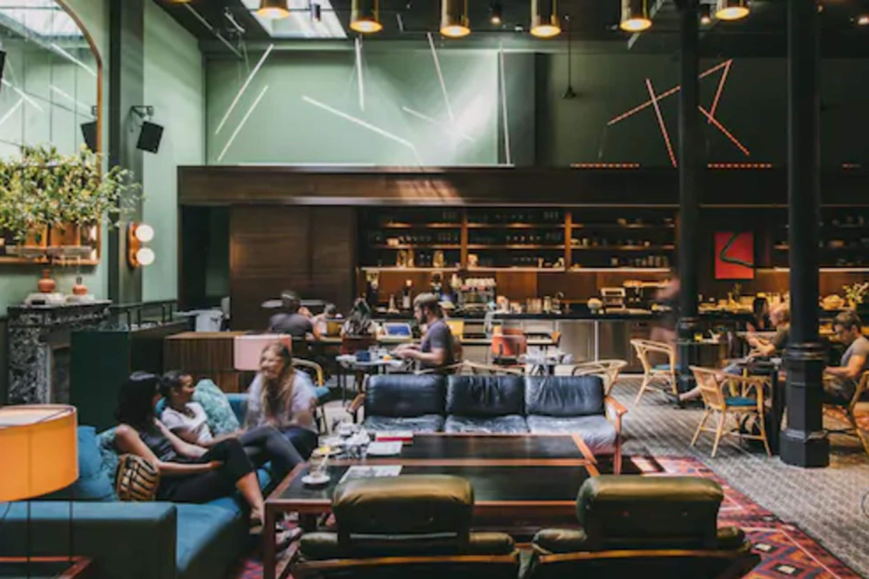 A spacious lounge area with leather seating, a bar area in the background, and a large window providing natural light.