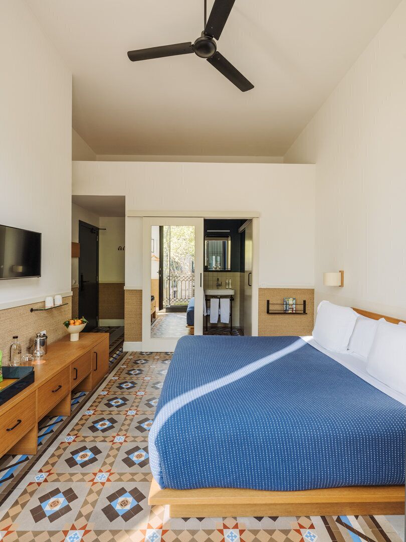 Un dormitorio con una cama, ventilador de techo, televisor, cómoda de madera y piso estampado.