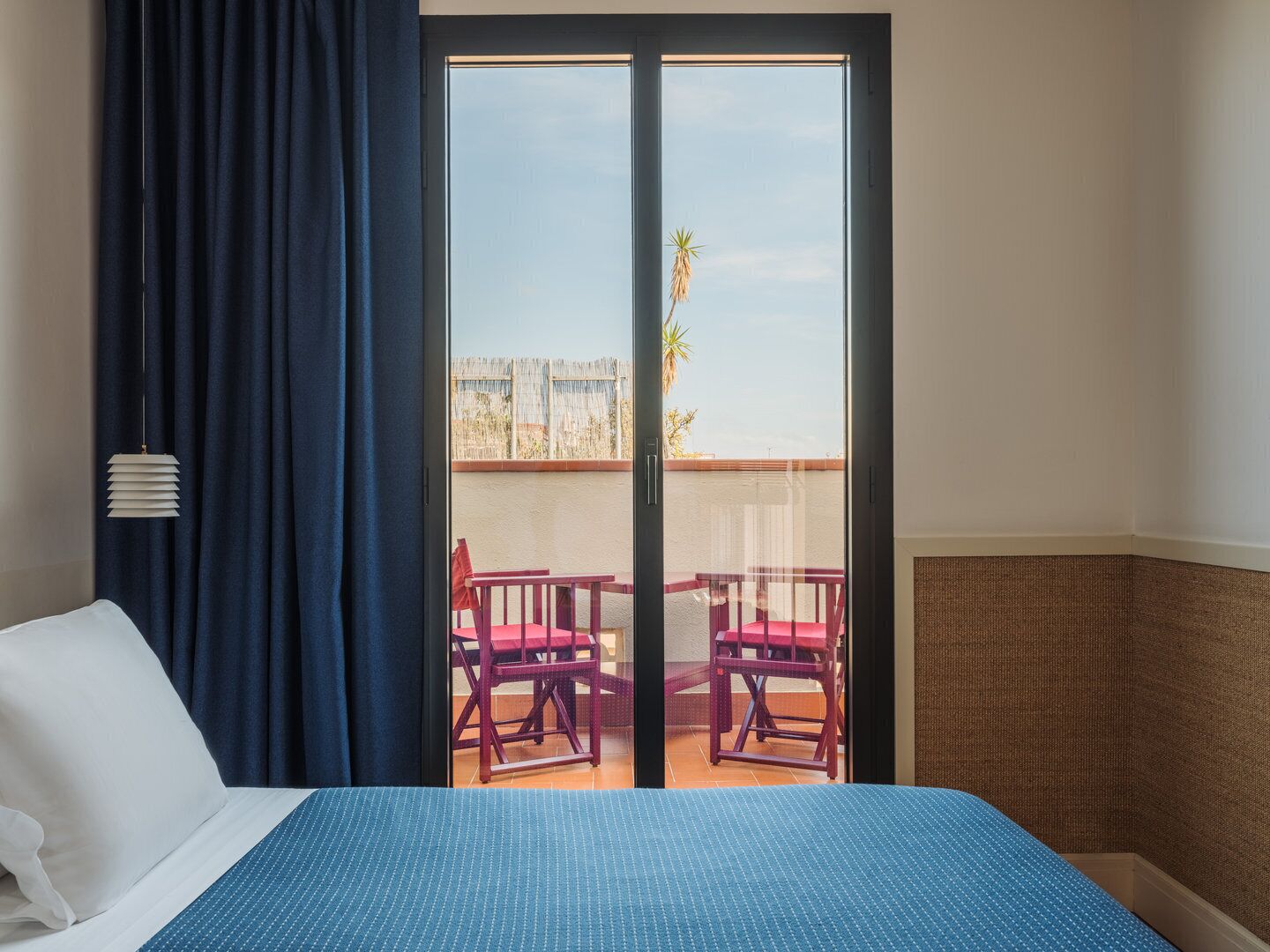 Una habitación de hotel con cama, ventana y vista a un balcón, además de una cortina.