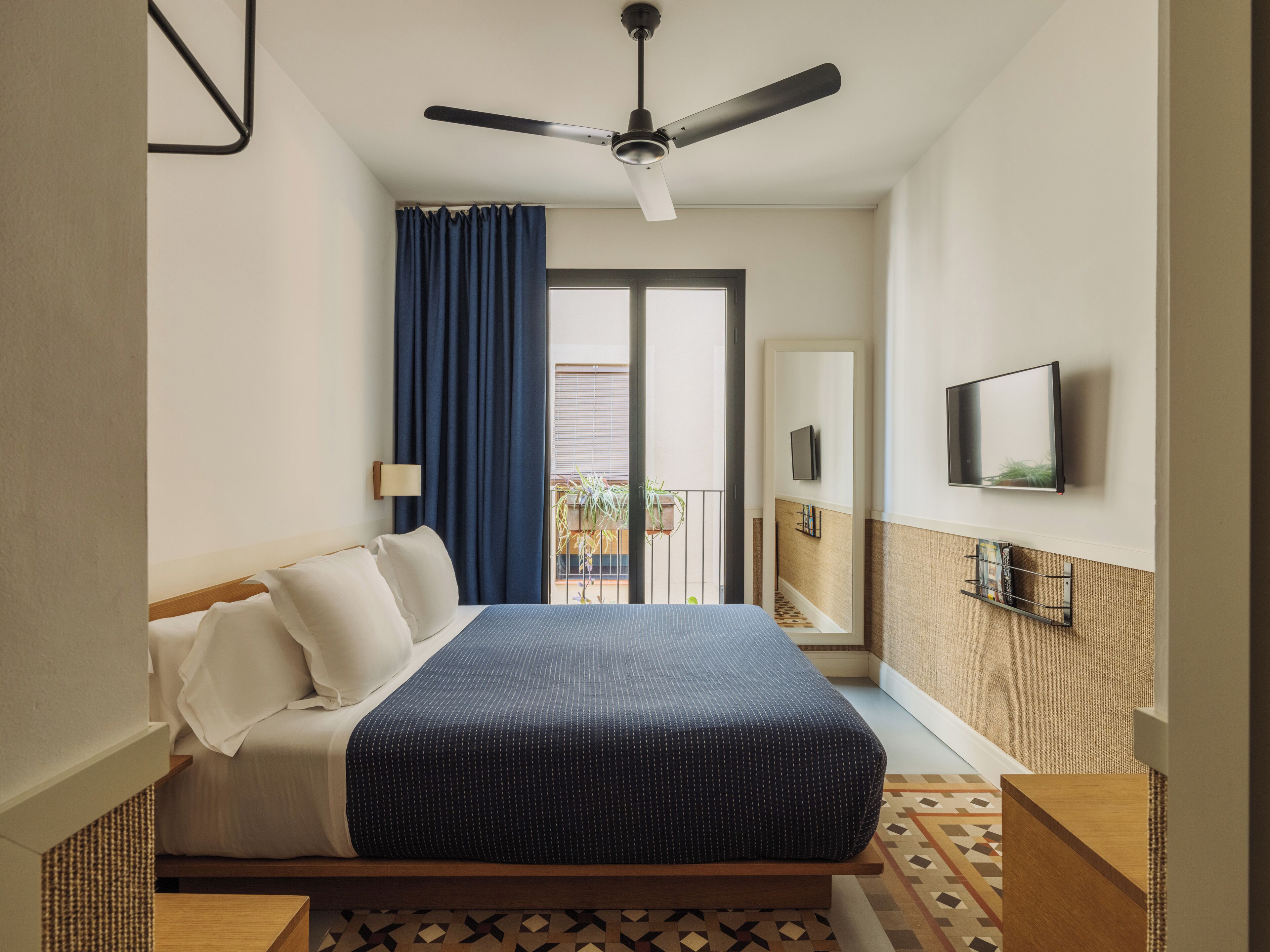 Quarto com cama, ventilador de teto, TV fixada na parede e varanda com vista.