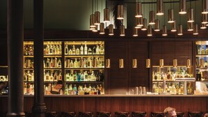 Un área de bar con diferentes opciones de asientos, incluyendo sillas de mimbre y un sofá, y una barra bien surtida con numerosas botellas.