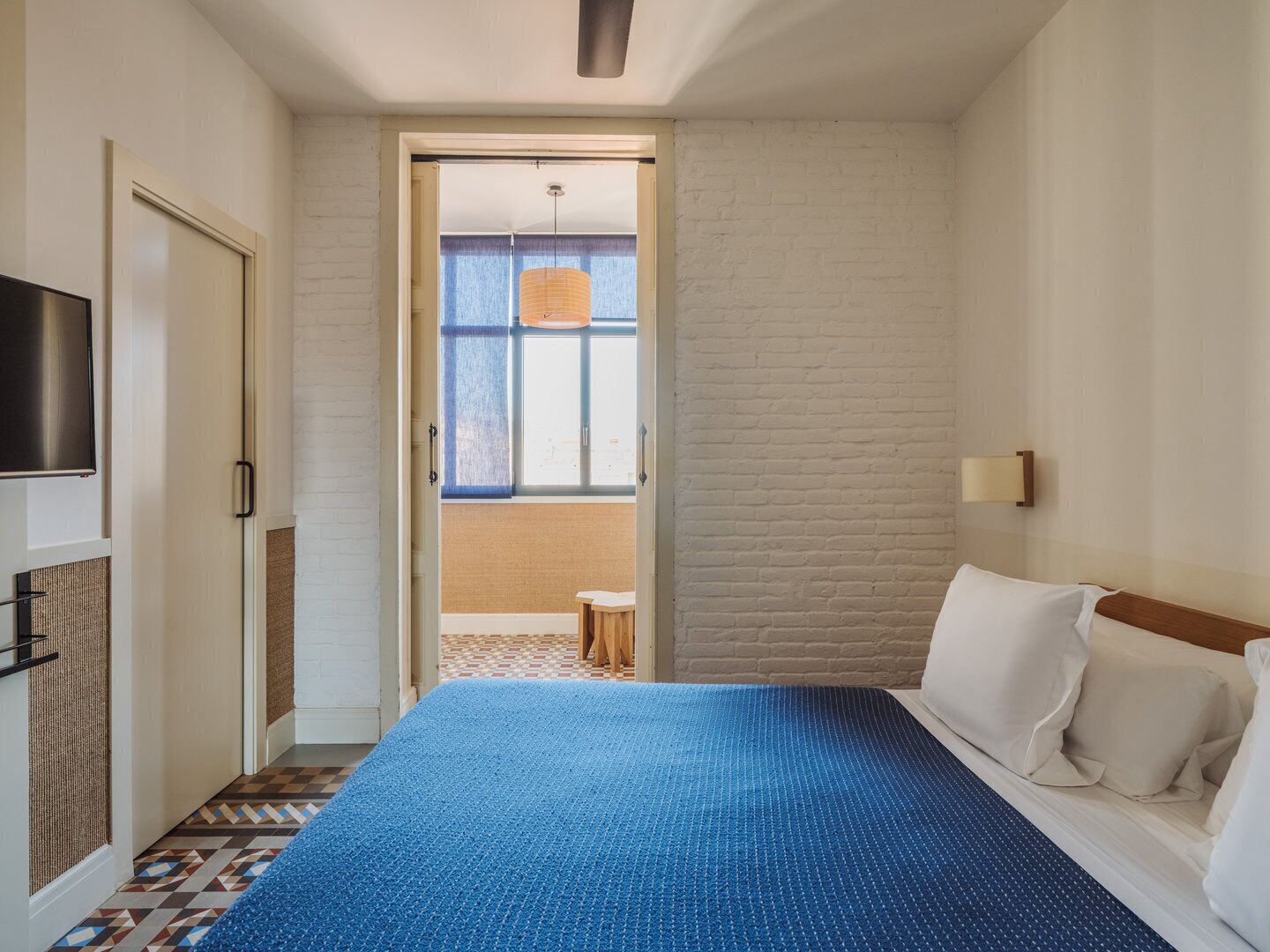 Habitación de hotel con cama, televisión, ventana con vistas y puerta que da a un balcón.
