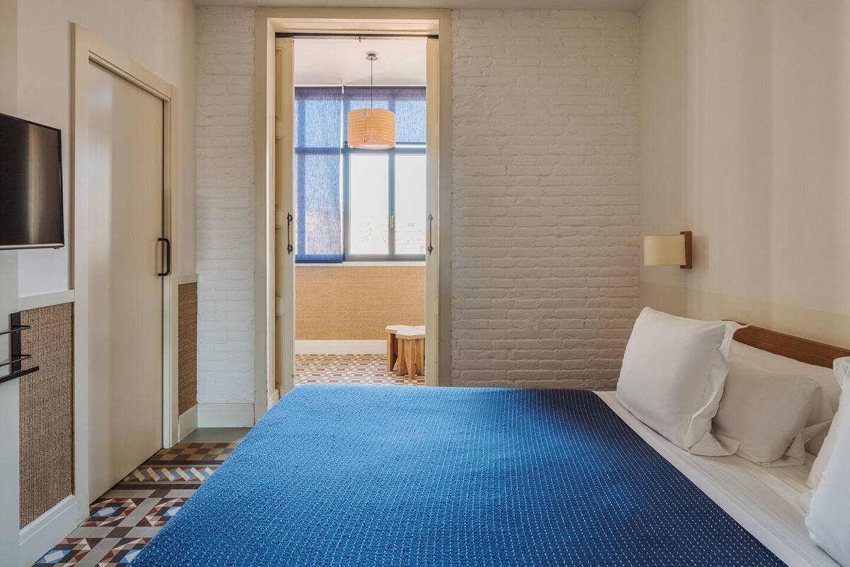 Une chambre d’hôtel avec un lit, une télévision, une fenêtre donnant sur un paysage agréable et une porte menant à un balcon.