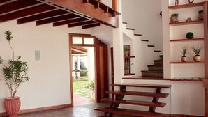 Una escalera de madera con peldaños que conducen a una plataforma, una planta en maceta y un estante con objetos decorativos.