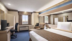 Et hotelværelse med en stor seng, et skrivebord med computer, en stol, et fjernsyn og et vindue med gardiner.