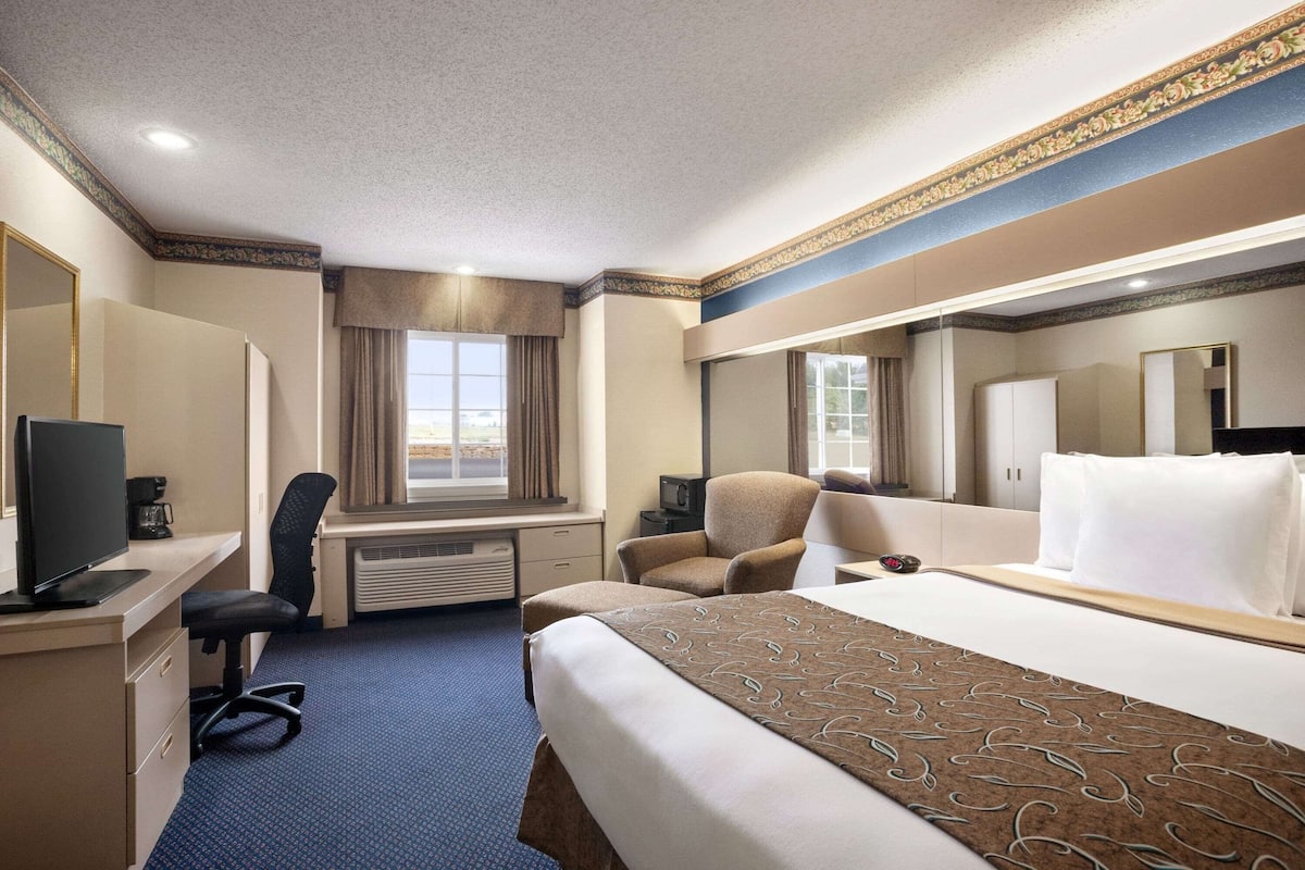 Quarto de hotel com cama grande, escrivaninha com computador, cadeira, televisão e janela com cortinas.