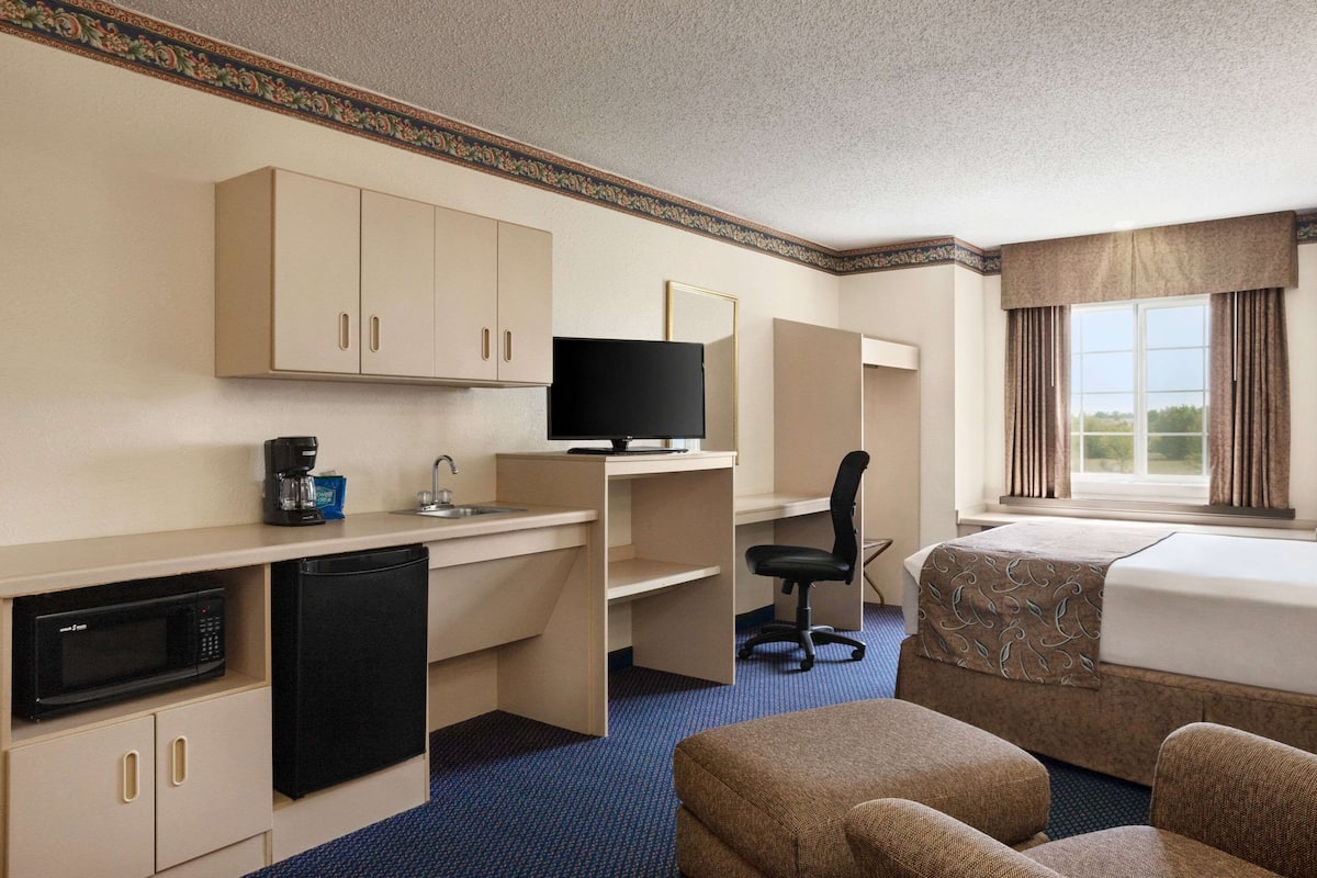 Quarto de hotel com cozinha compacta, uma cama, escrivaninha e televisão.